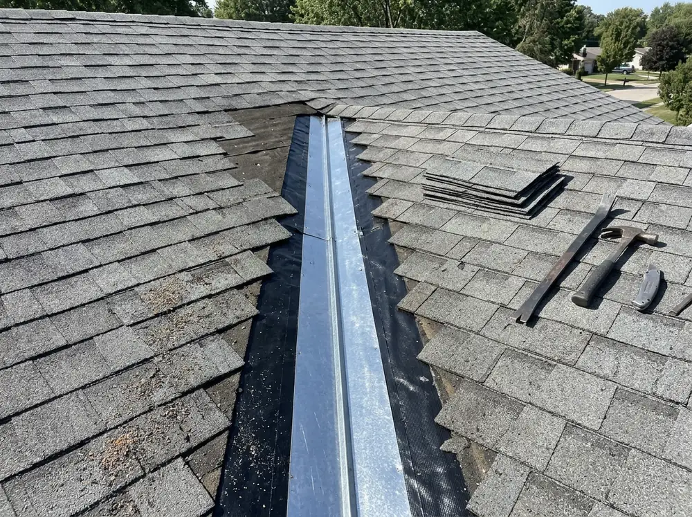 Shingles lifted along a roof valley to expose new metal valley flashing and underlayment